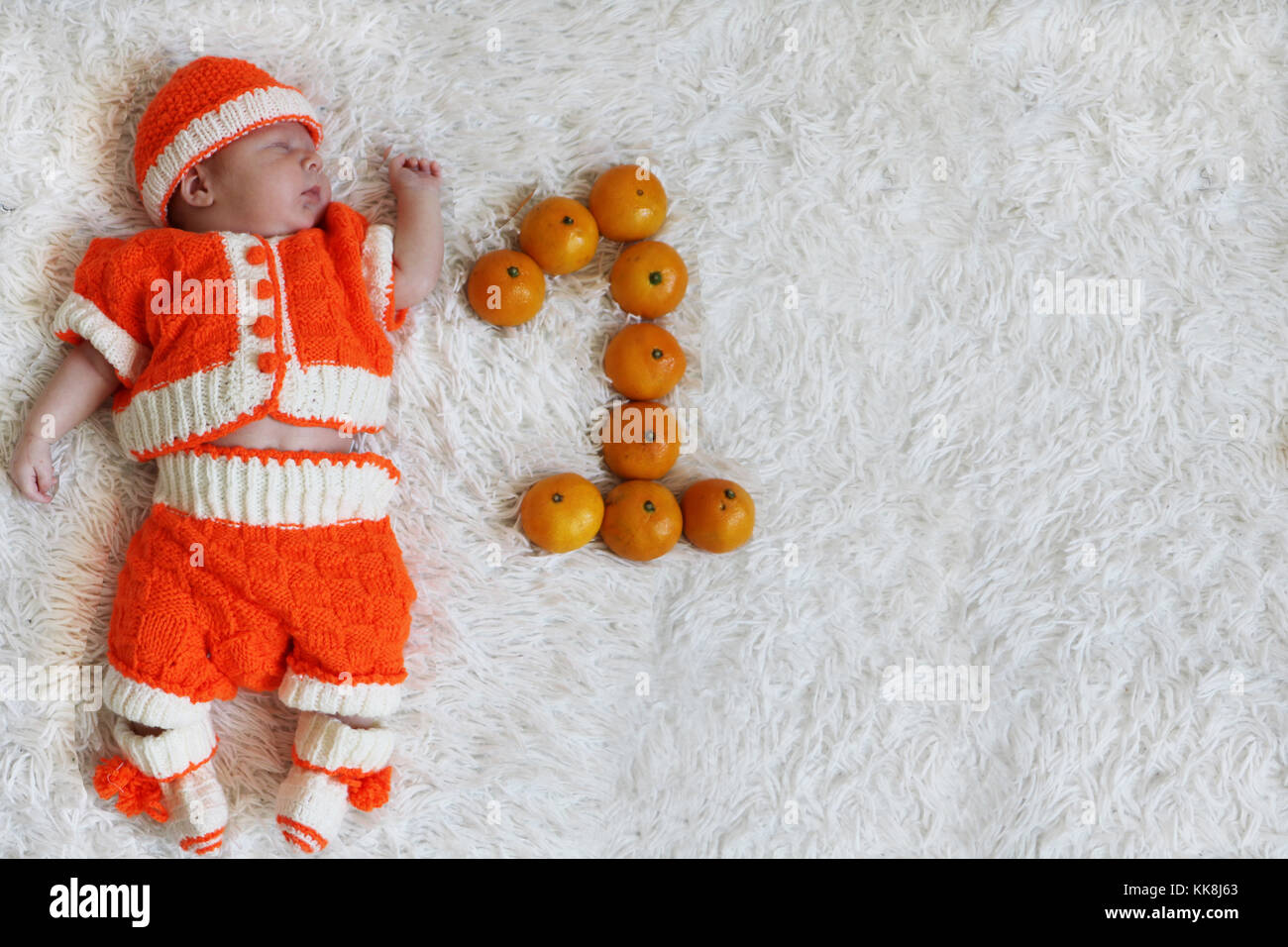 Bébé d'un mois. Dormir bébé nouveau-né un mois à orange en costume sur la fourrure blanche couverture avec un chiffre à côté de lui et l'espace pour le texte. Banque D'Images