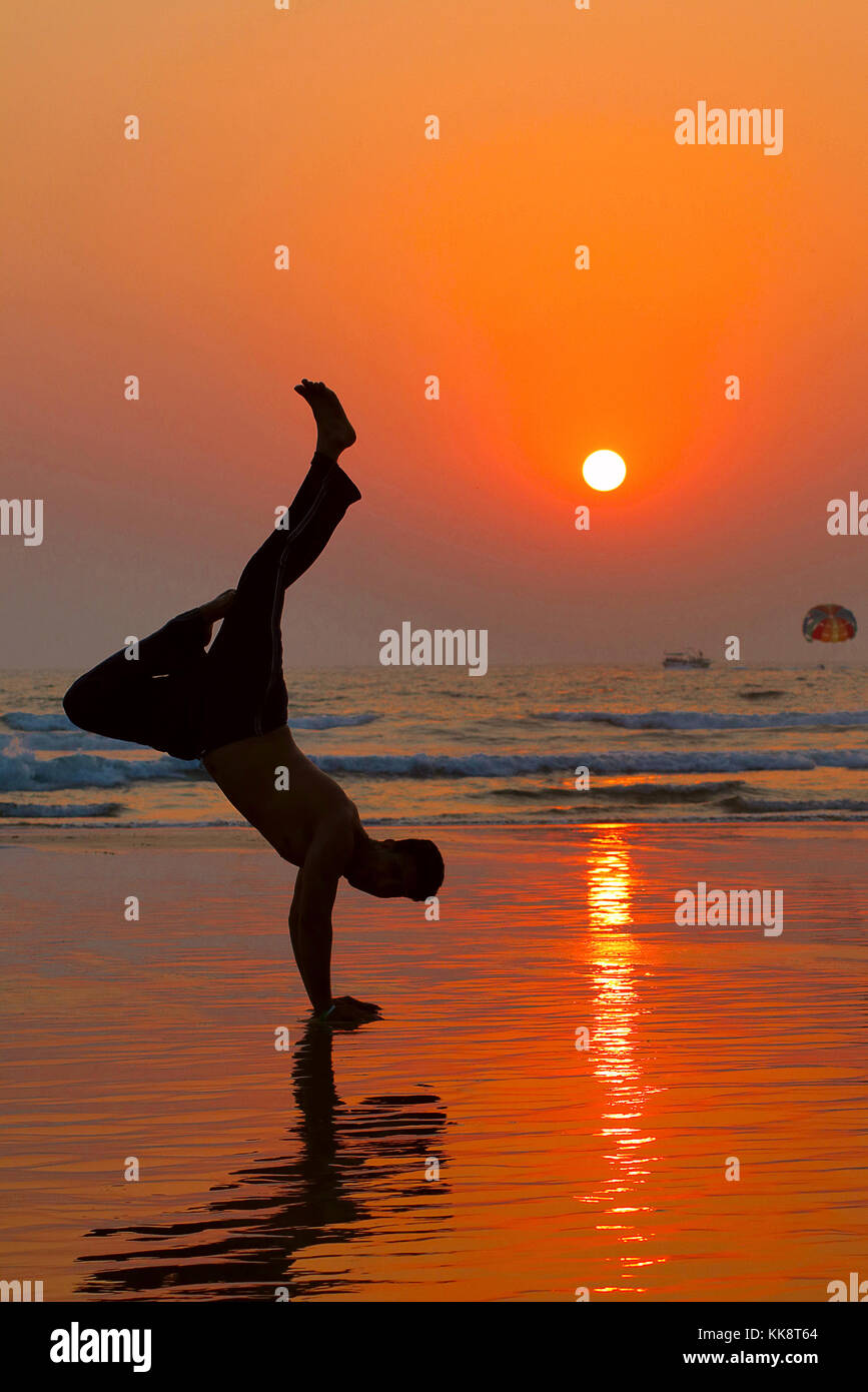 Jeune homme dans une posture hip hop, équilibre à la main, jambes en l'air sur la plage au coucher du soleil Banque D'Images