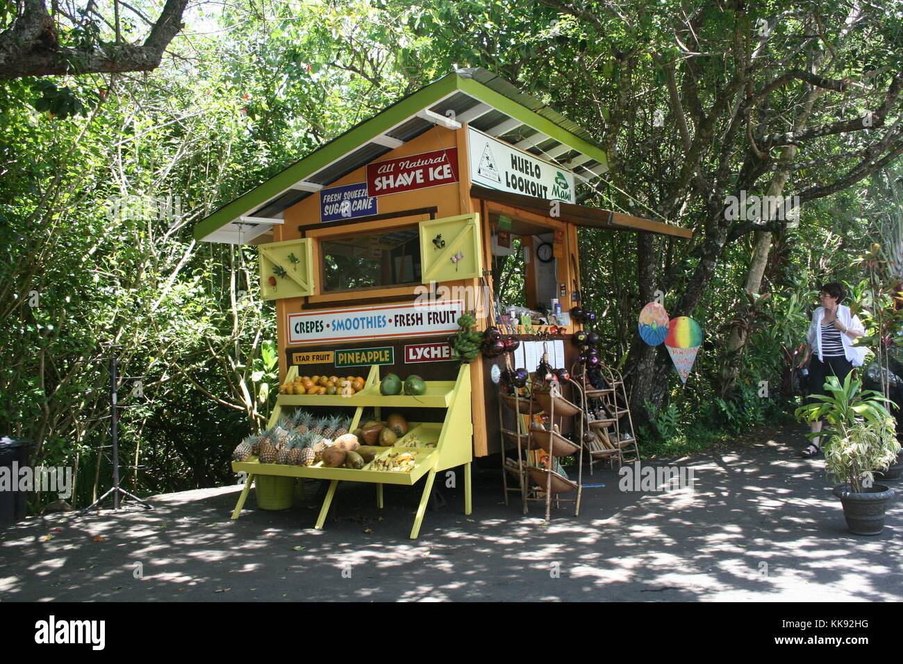 Une photographie de l'Huelo Lookout Stand de fruits sur la route de Hana, les produits frais peuvent être vus exposés à la vente à l'extérieur du stand, un touriste est à la recherche sur le stand qui est situé sur le bord d'une route le long d'une zone densément boisée, Maui, Hawaii, 2014. Banque D'Images