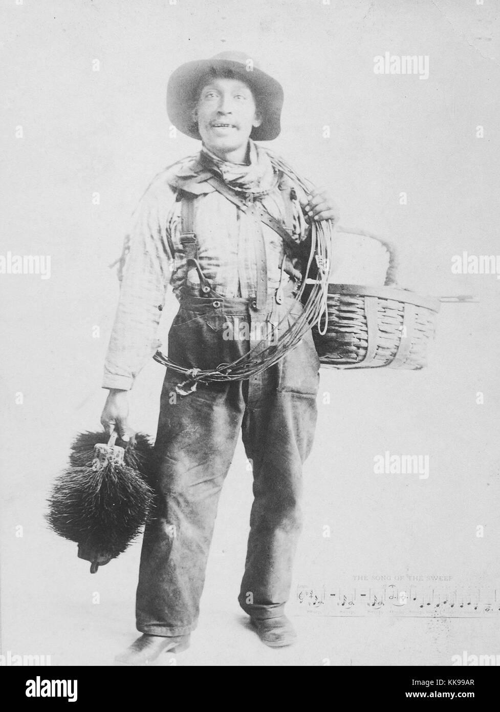 Sepia studio portrait d'un homme afro-américain, pleine longueur, pleine de vêtements ramoneur, tenant un panier, des câbles et des balayeuses, 1900. À partir de la Bibliothèque publique de New York. Banque D'Images