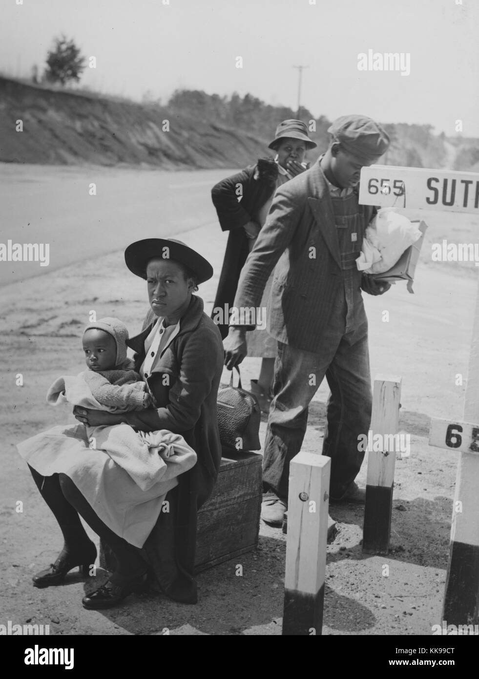 Photographie en noir et blanc d'une famille afro-américaine, un homme debout, une femme assise tenant un bébé, et a mature woman standing en arrière-plan, en attente sur le côté de la route, comté de Halifax, en Virginie, Mars, 1941. À partir de la Bibliothèque publique de New York. Banque D'Images