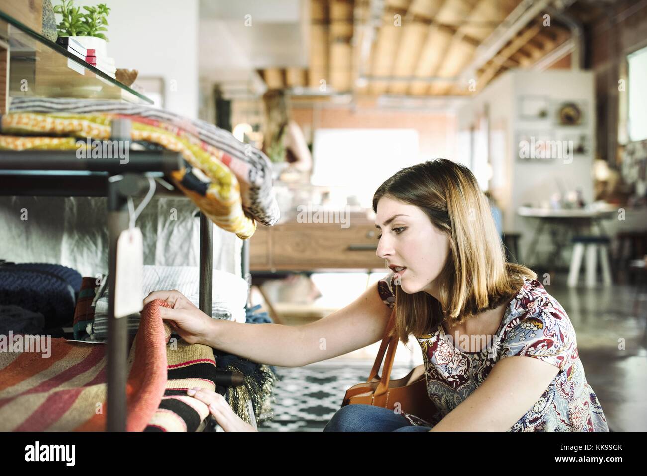 Jeune femme dans un magasin, regardant des tapis sur une étagère. | utilisation dans le monde entier, libre de droits : pour le prix d'utilisation comercial sur demande. Banque D'Images