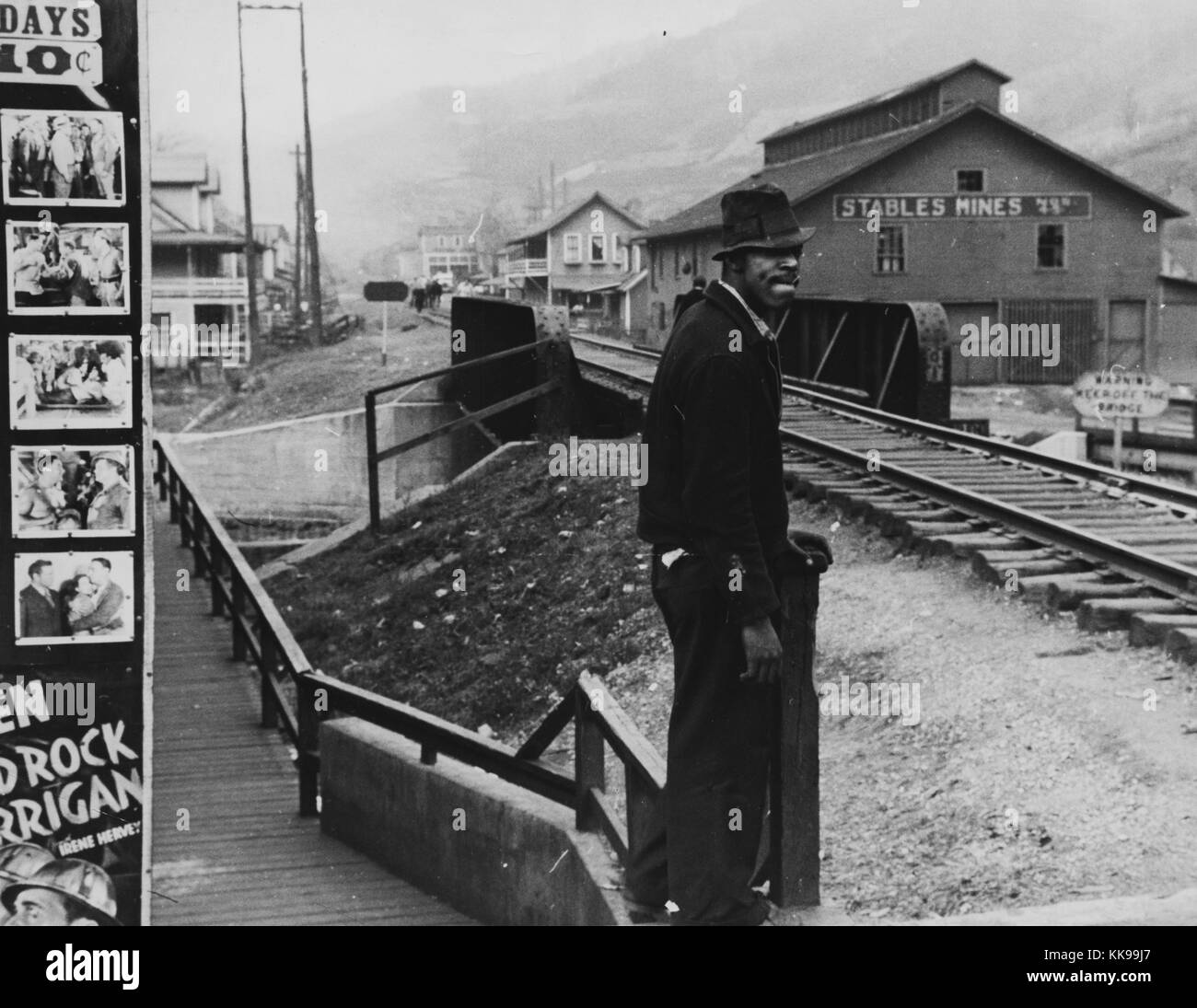 Photographie en noir et blanc d'un homme afro-américain, portant une chemise et un chapeau, debout à un arrêt de train, les bâtiments peuvent être vus dans l'arrière-plan, Omar, West Virginia, 1935. À partir de la Bibliothèque publique de New York. Banque D'Images