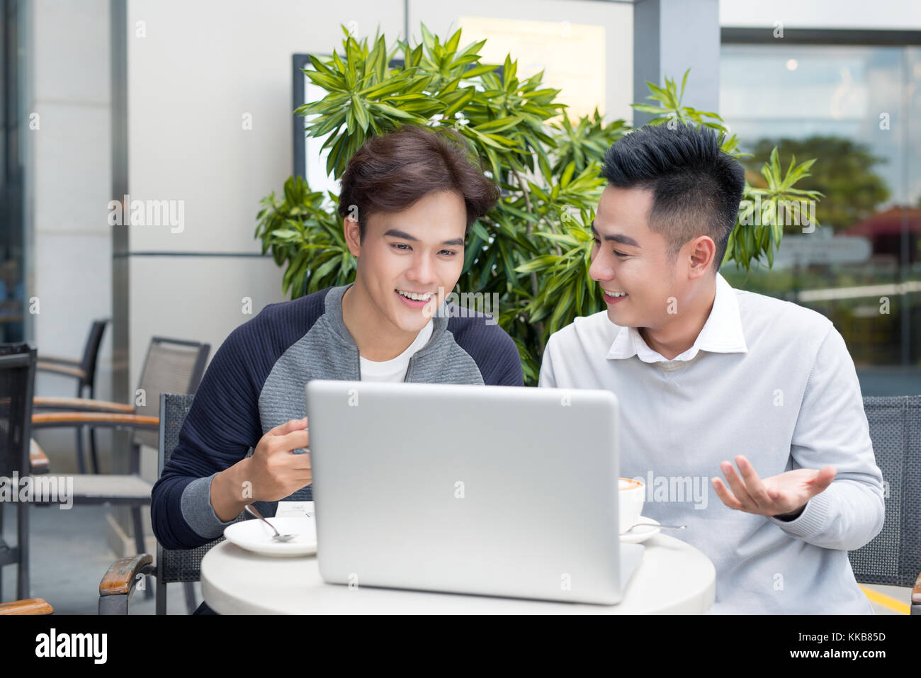 Deux hommes d'affaires de rire tout en ayant une rencontre dans un café classique exposée, à l'aide d'un ordinateur portable. Banque D'Images