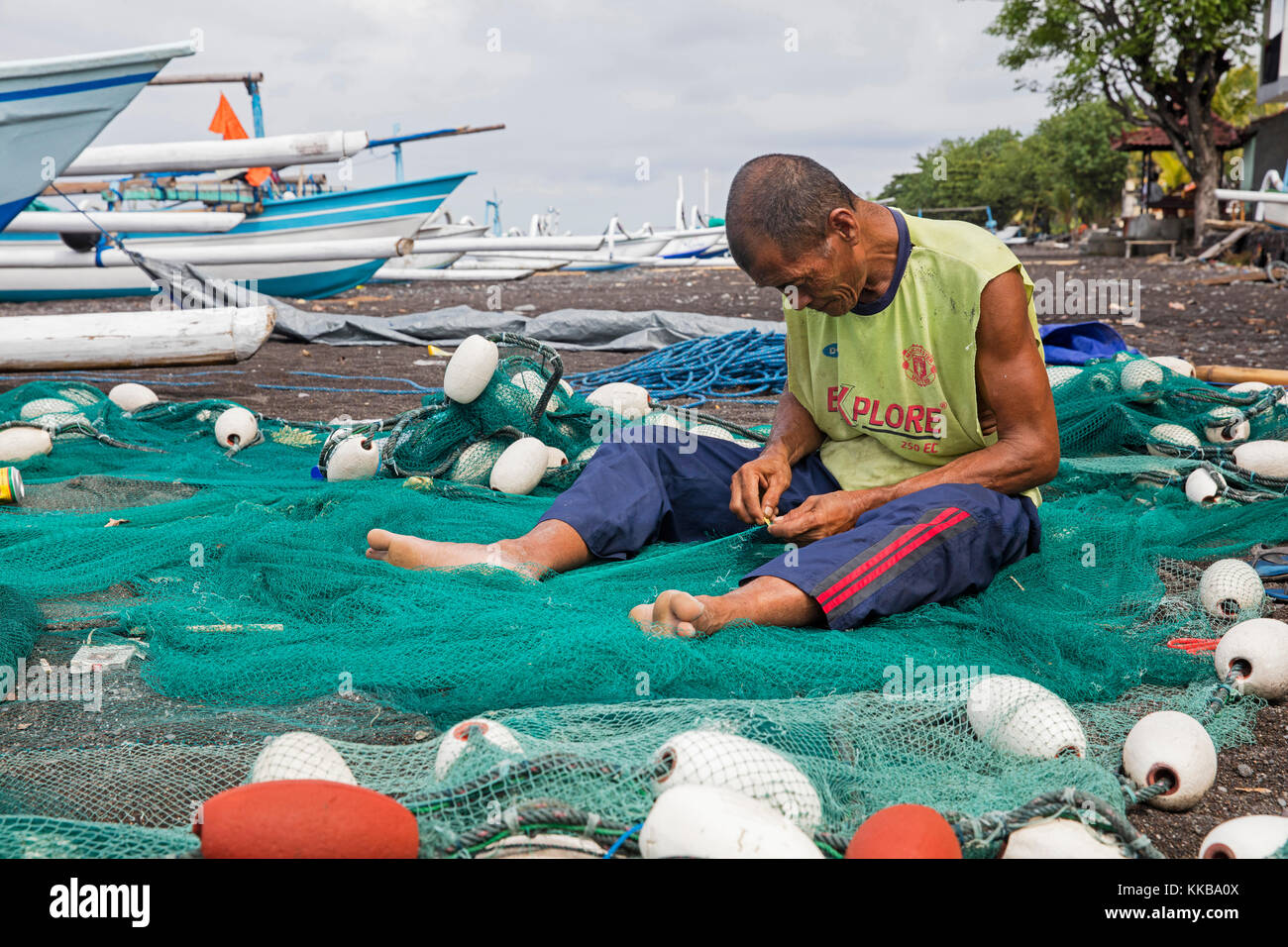 La réparation de filet de pêche pêcheur balinais / résille sur le sable volcanique noir d'amed beach sur l'île de Bali, Indonésie Banque D'Images