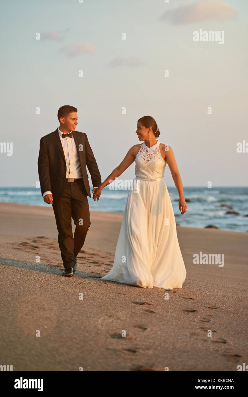 Heureux marié et mariée à pied sur la plage au coucher du soleil la lumière Banque D'Images