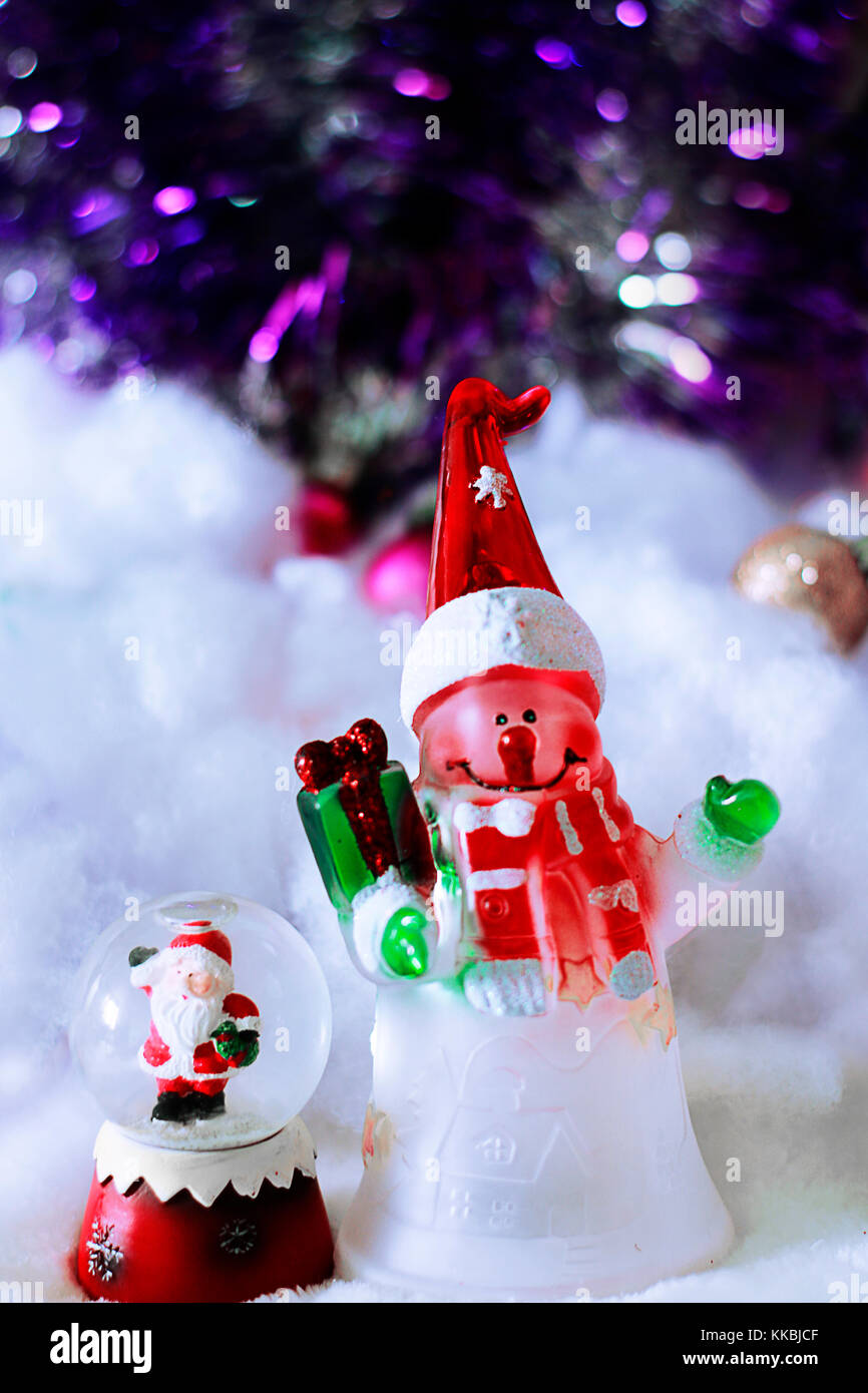 Jouets mignon de snowman in santa hat avec don et le père Noël en boule de cristal sur fond neigeux floue flou artistique avec tresse. Banque D'Images