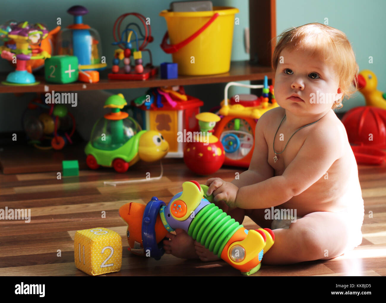 Mignon petit bambin avec ginger hair assis sur le sol au milieu des jouets en plastique holding dog dans les mains. Banque D'Images