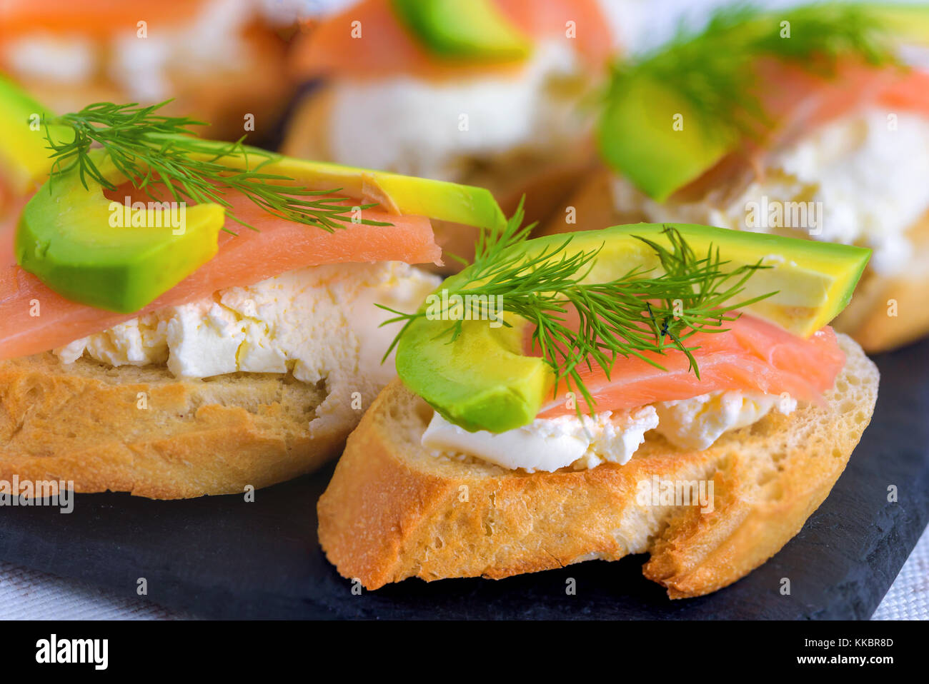 Bruschetta, snack-sandwiches avec du fromage blanc, saumon fumé et morceaux d'avocat décoré par de l'aneth. Banque D'Images