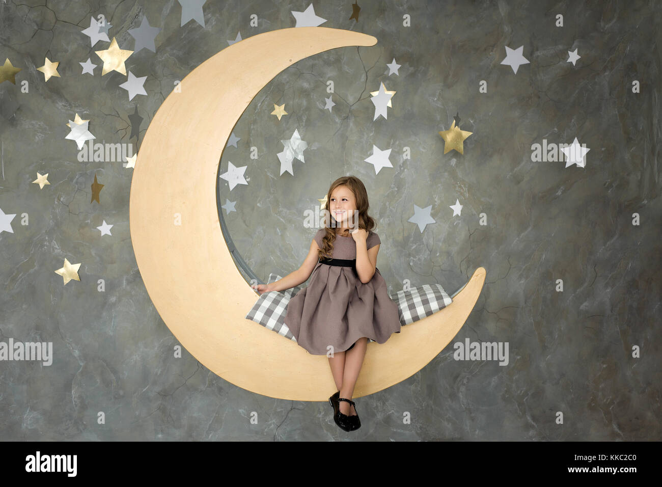 Petite fille en robe grise est assis sur grande lune. Petite fille à rêver Banque D'Images