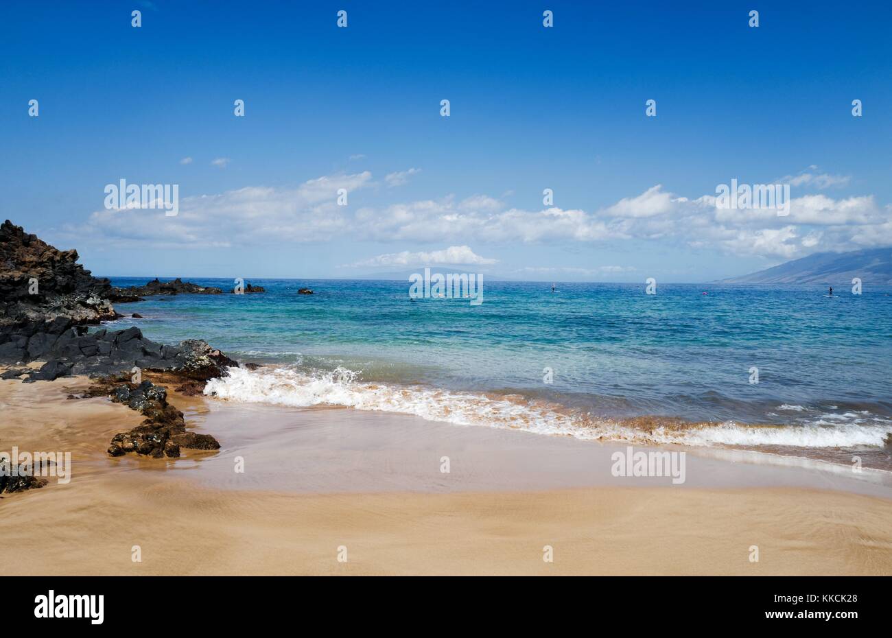 Lors d'une journée ensoleillée à la plage de Wailea, petites vagues casser sur le sable près de roches volcaniques, en tant que touristes tuba et l'utilisation du stand up paddle boards, Wailea, Maui, Hawaii, 2016. Banque D'Images