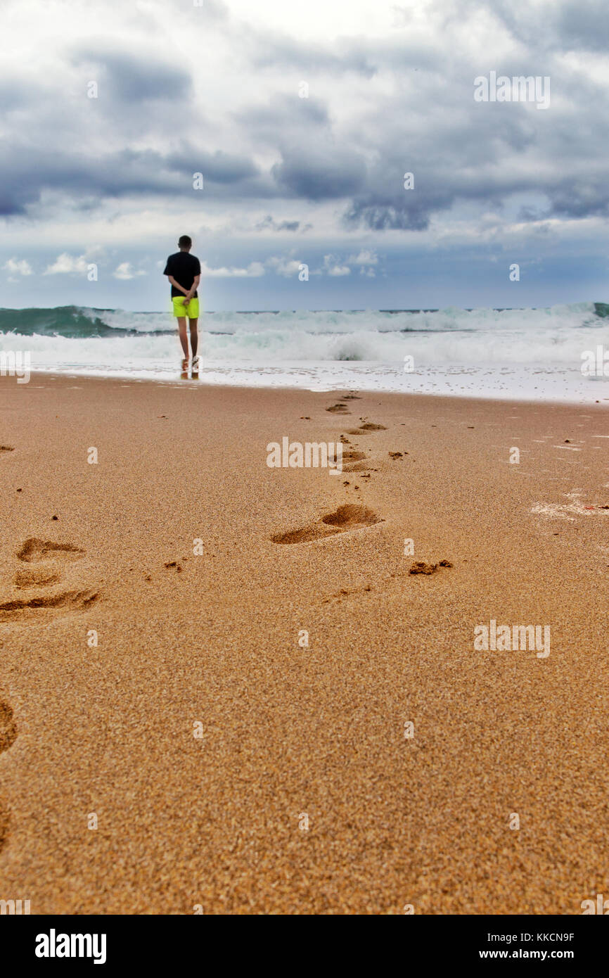Des traces sur la plage de sable par la mer au cours de l'assaut du mauvais  temps. sur la frontière de sable et l'eau il y a un jeune homme en short