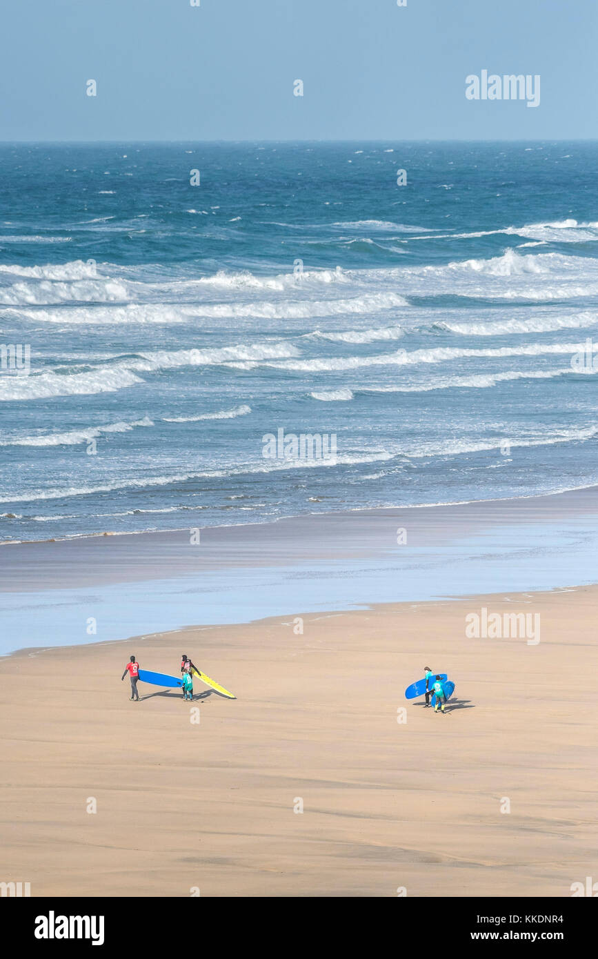 Surf - instructeurs d'une école de surf école de surf et les jeunes apprenants à pied de la mer et portant leurs planches de surf à la plage de Fistral Newquay. Banque D'Images