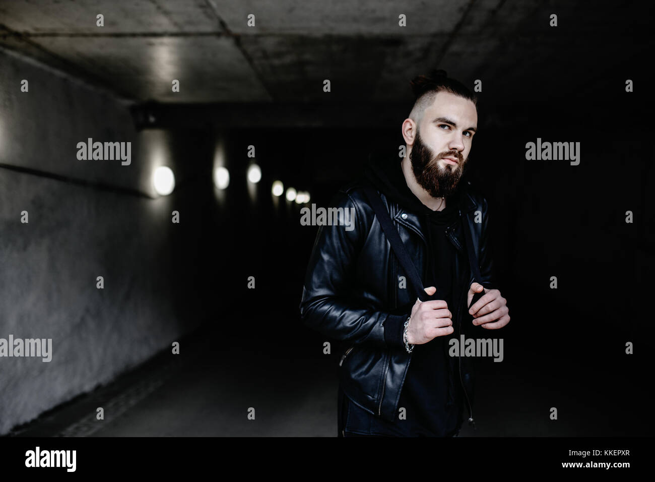 Jeune homme barbu moderne en noir vêtements de style debout dans autour d'origine urbaine. Banque D'Images Jeune homme barbu moderne en noir vêtements de style debout dans autour d'origine urbaine. Banque D'Images