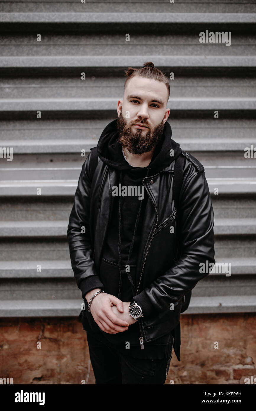 Jeune homme barbu moderne en noir vêtements de style debout dans autour d'origine urbaine. Banque D'Images Jeune homme barbu moderne en noir vêtements de style debout dans autour d'origine urbaine. Banque D'Images