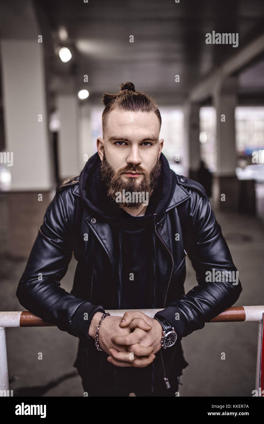 Jeune homme barbu moderne en noir vêtements de style debout dans autour d'origine urbaine. Banque D'Images Jeune homme barbu moderne en noir vêtements de style debout dans autour d'origine urbaine. Banque D'Images