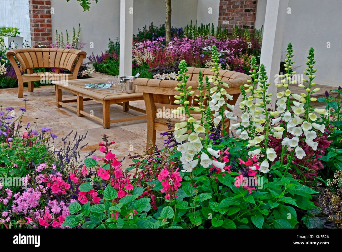 Un jardin contemporain avec terrasse et un élégant mobilier en bois entouré de fleurs colorées frontières Banque D'Images