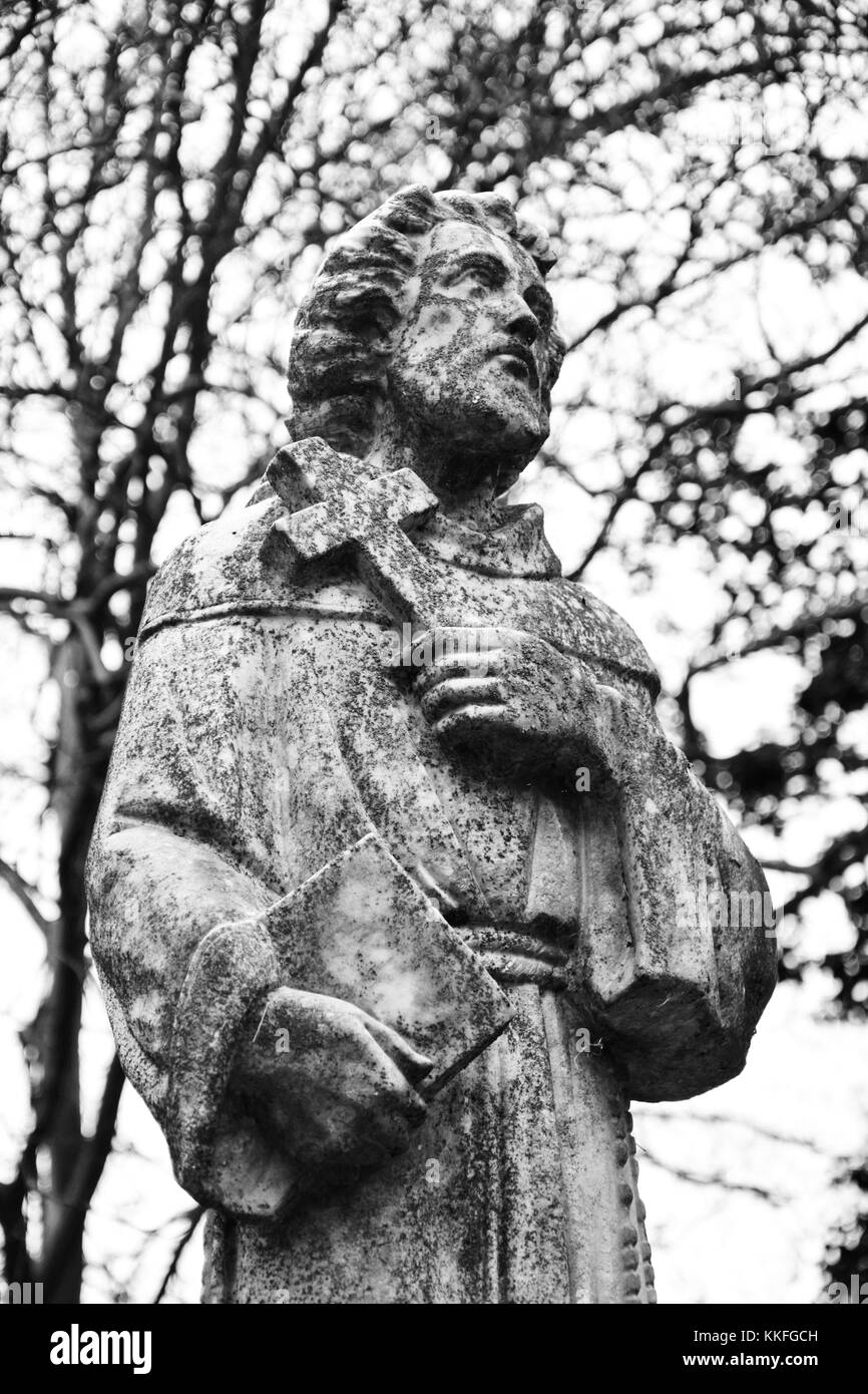 Statue d'un moine catholique tenant une bible et une croix au sommet d'un tombeau. Banque D'Images