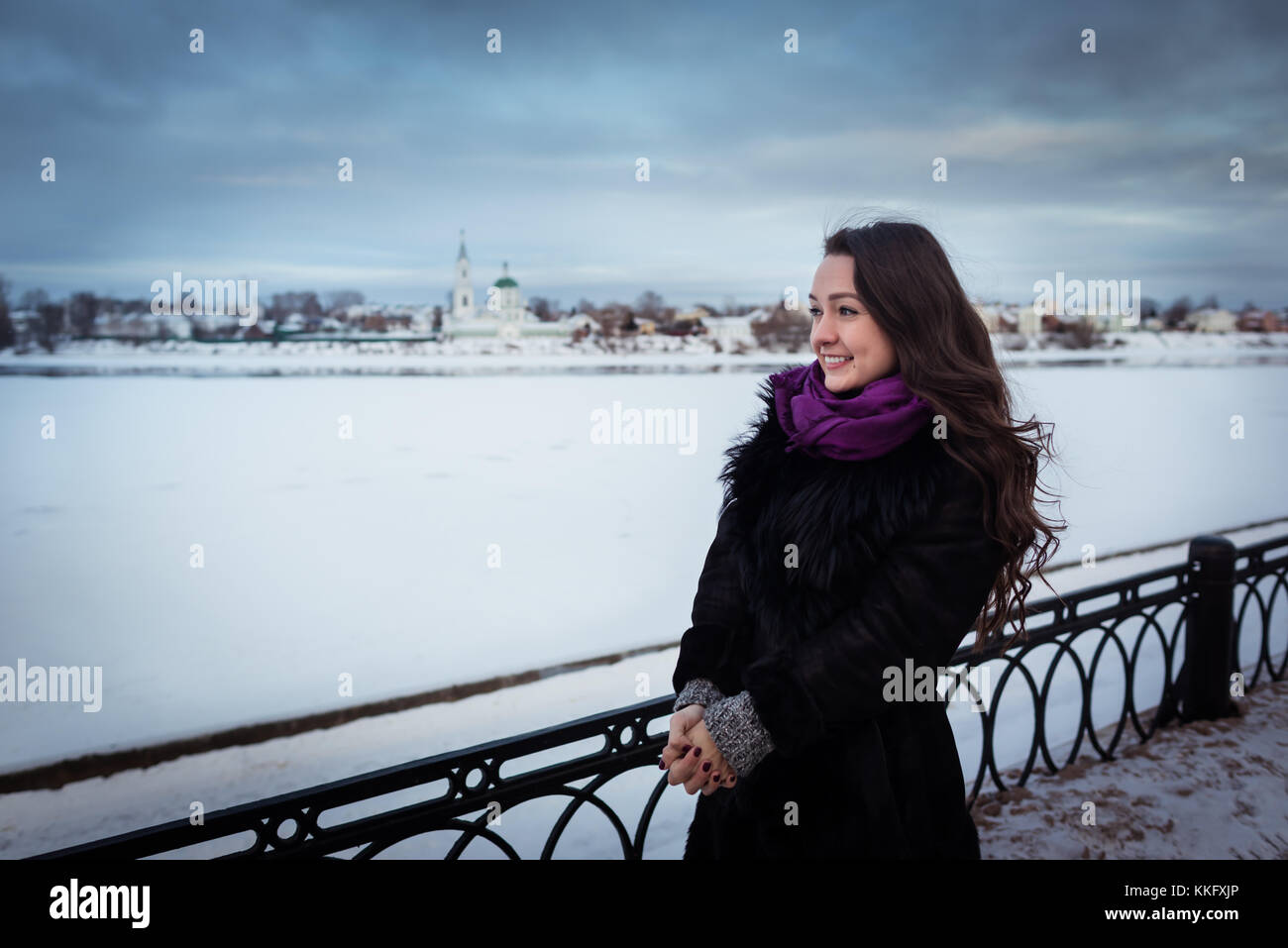 Jeune femme avec de beaux cheveux longs en écharpe pourpre, debout près de la Snowy River sur la promenade de la ville et à la recherche de l'hôtel. journée froide, ciel nuageux Banque D'Images