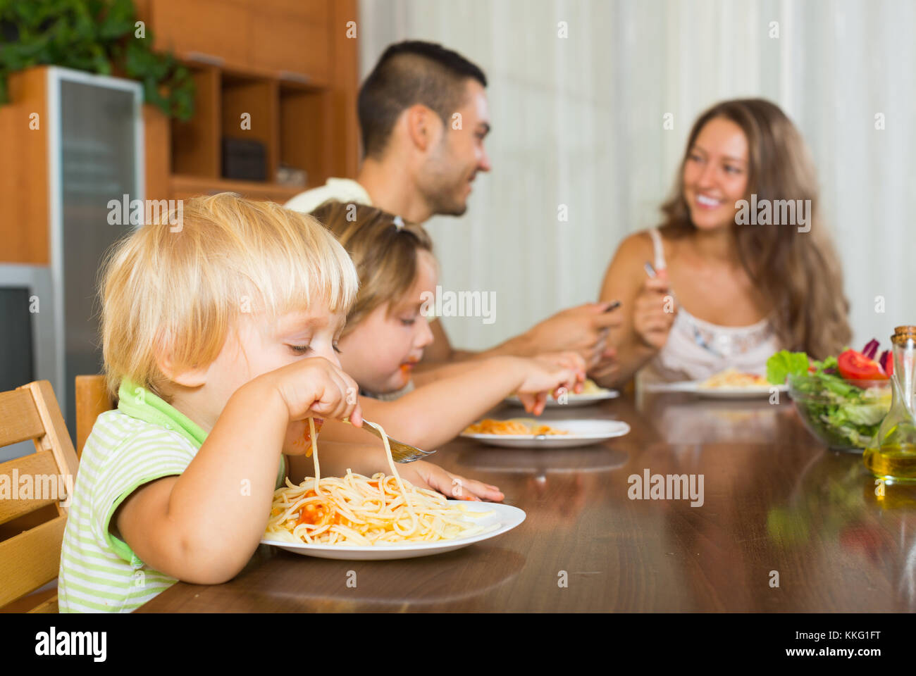Smiling young positive famille de quatre personnes en train de déjeuner avec les spaghettis à la maison Banque D'Images