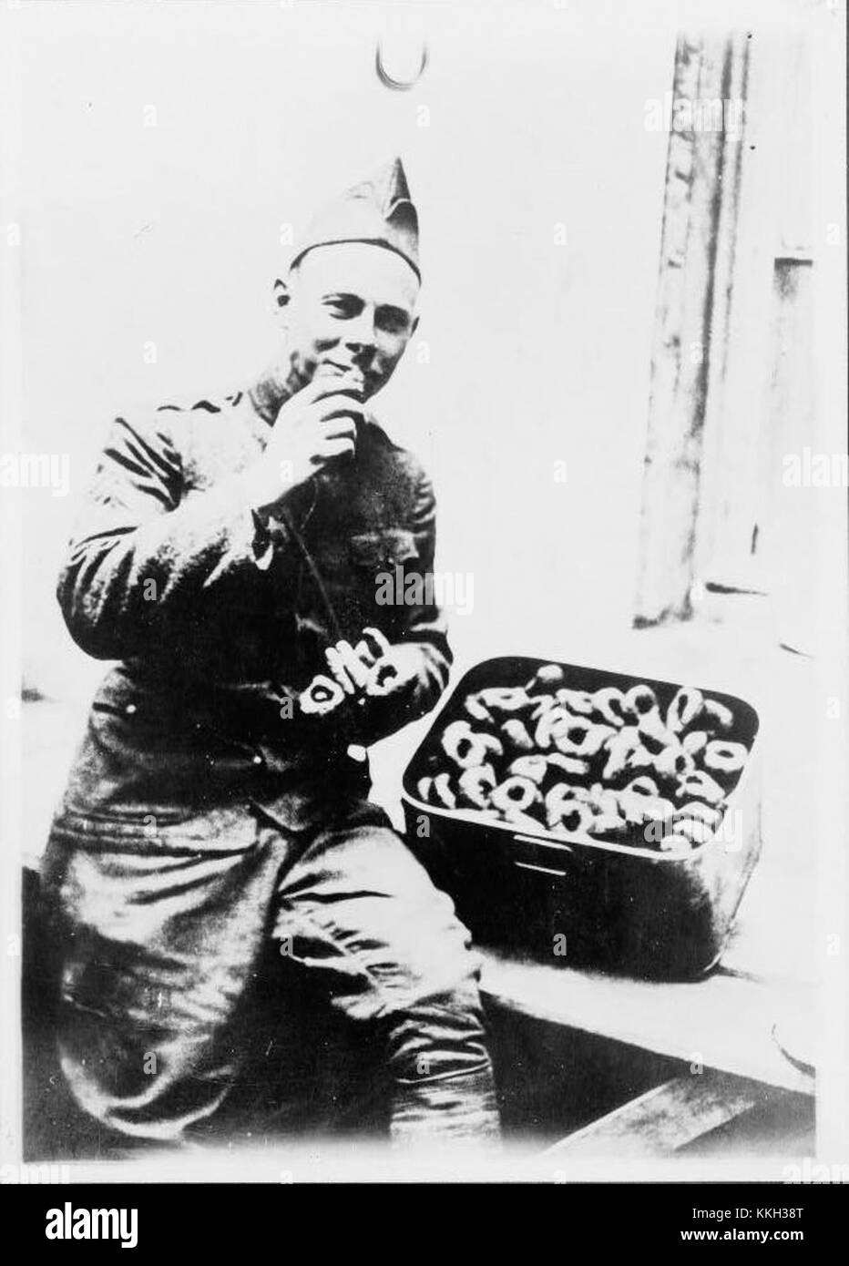 Cette image montre un soldat américain mangeant des beignets, probablement pendant la première Guerre mondiale, les beignets sont devenus un symbole de confort à la maison et de soutien pour les soldats, en particulier pendant les efforts de guerre tels que les Donut Dollies qui servaient des beignets aux troupes. Banque D'Images