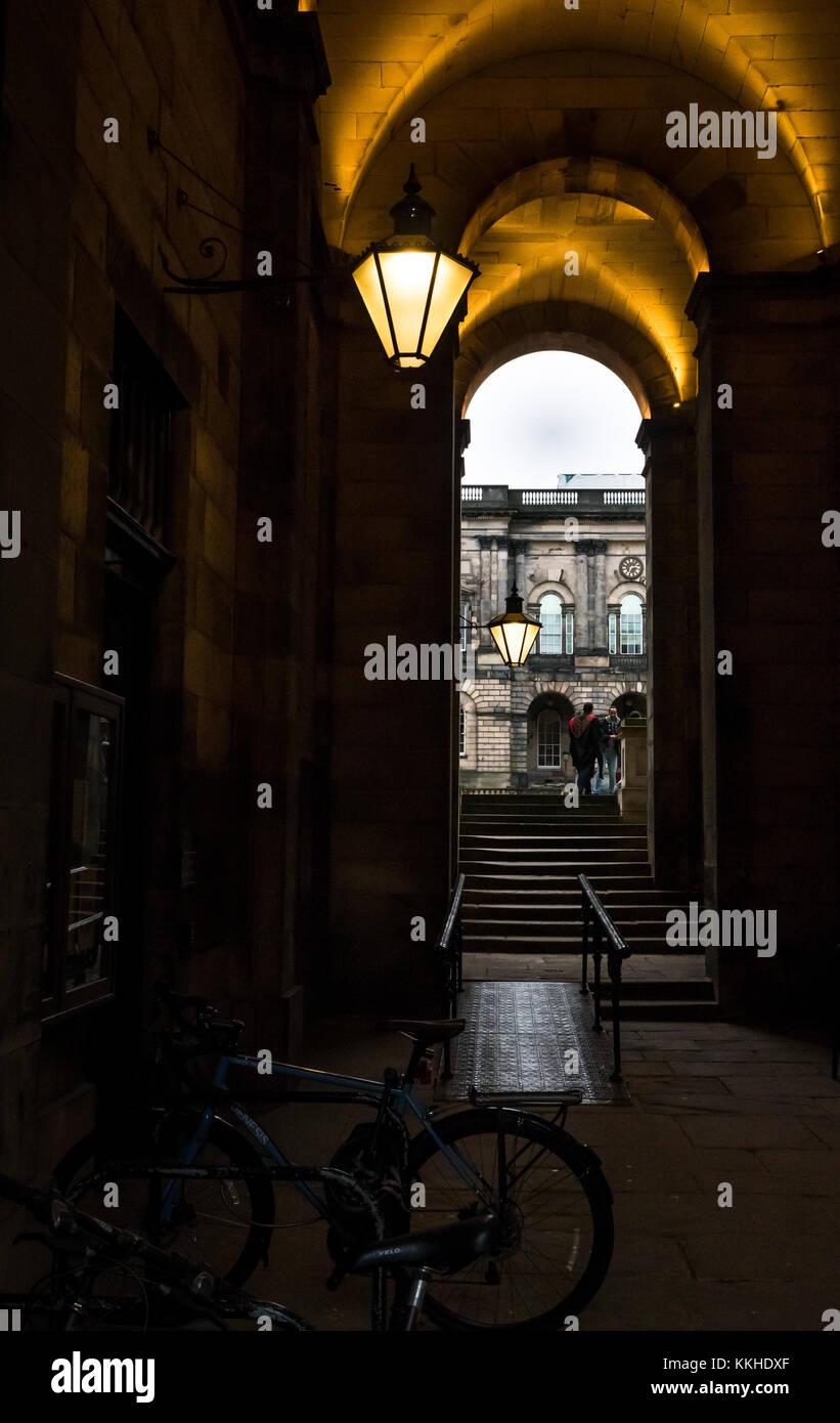 Edinburgh, Ecosse, Royaume-Uni. 1er décembre 2017. Un étudiant de graduation gown dans Old College, cour intérieure du pont sud, Université d'Édimbourg, avec des lampes de style Victorien allumé dans le noir après-midi dans le couloir extérieur Banque D'Images