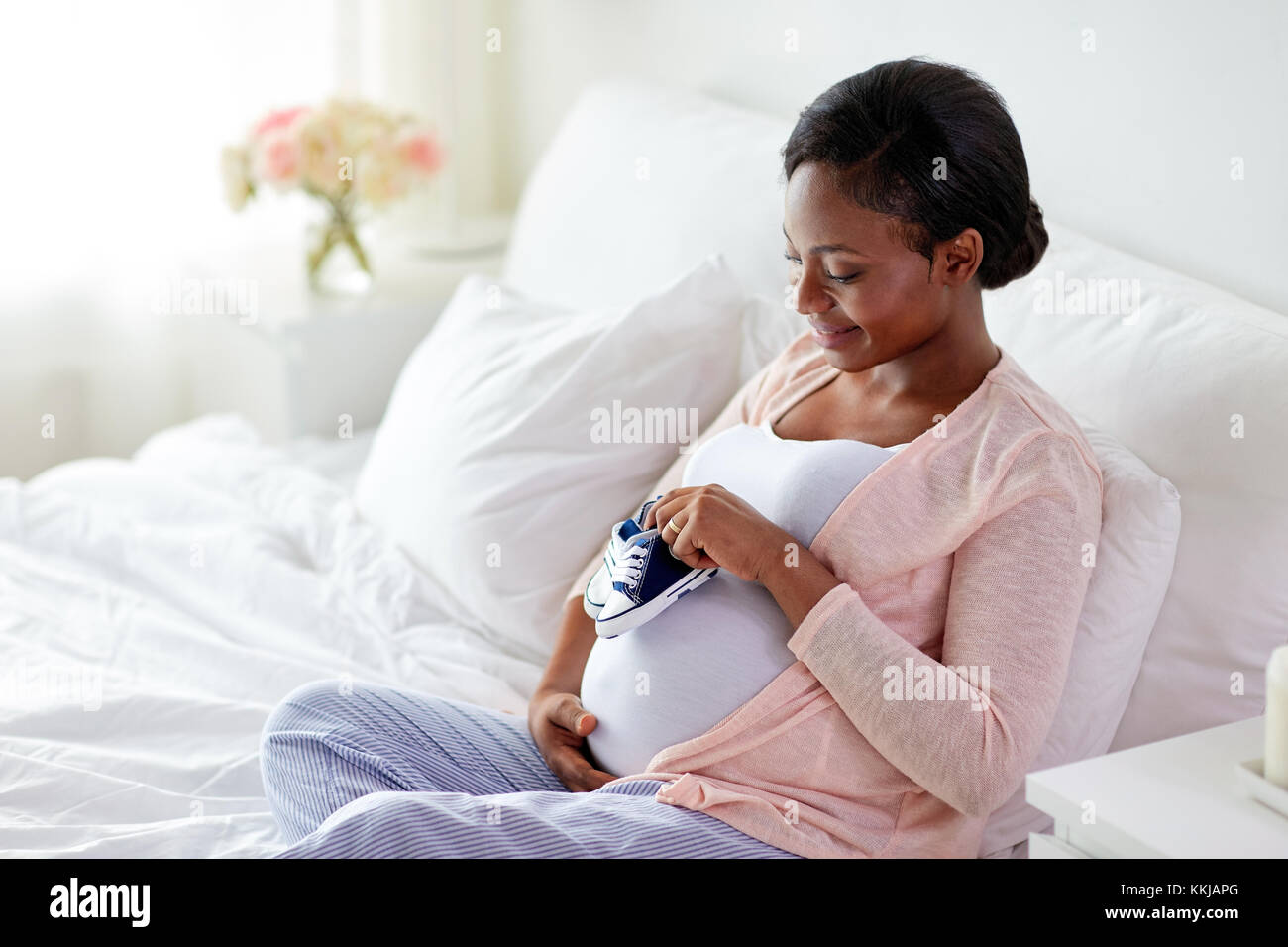 Pregnant african woman avec chaussons bébé au lit Banque D'Images