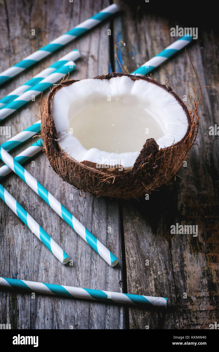 Broken coconut avec du lait de coco et cocktail vintage tubes sur la vieille table en bois. voir la série Banque D'Images