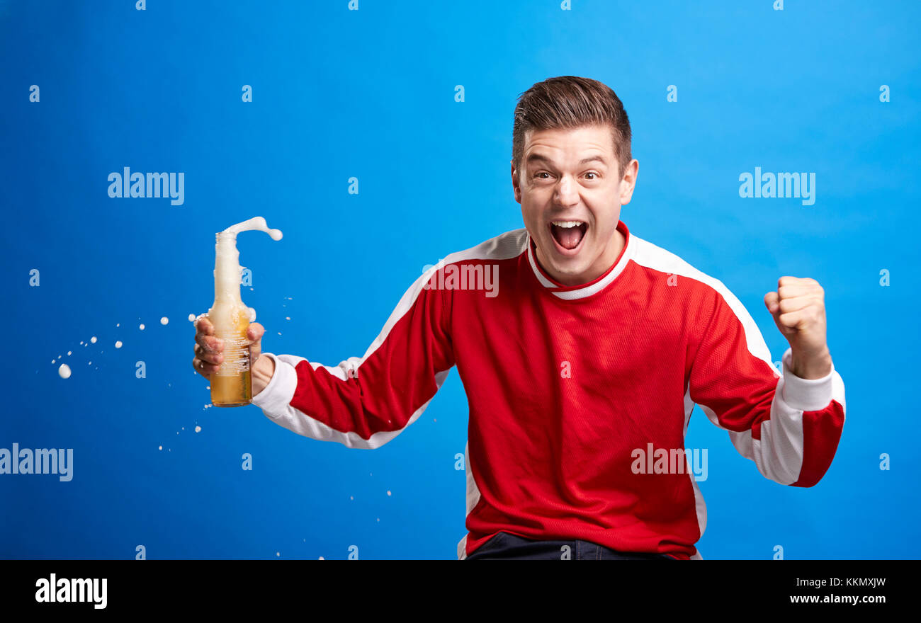 Jeune homme sports fan de célébrer avec une boisson déversant Banque D'Images