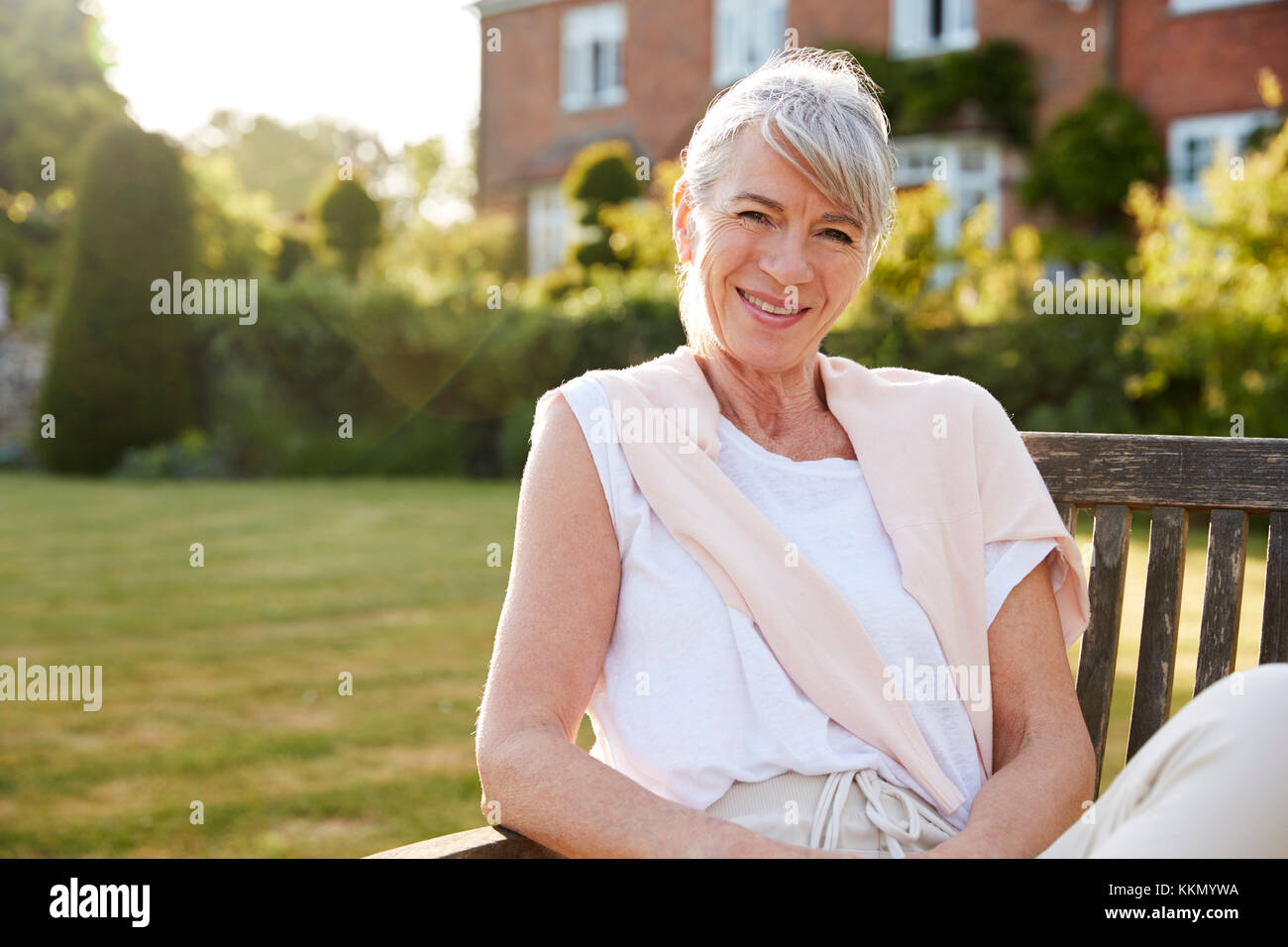 Senior Woman Sitting on Banc de jardin à la lumière du soleil du soir Banque D'Images