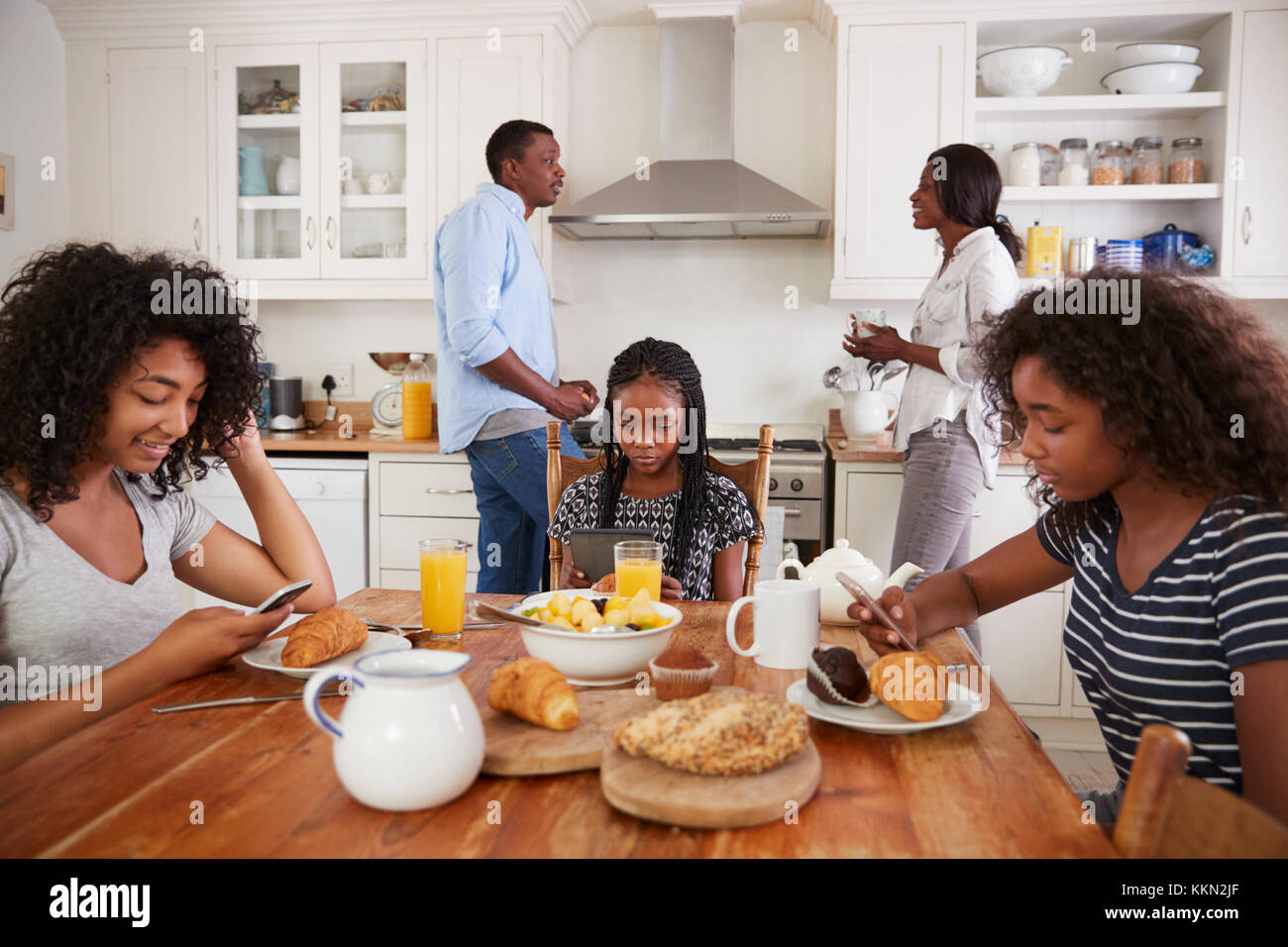 Famille assis autour d'une table de petit-déjeuner à l'aide d'appareils numériques Banque D'Images
