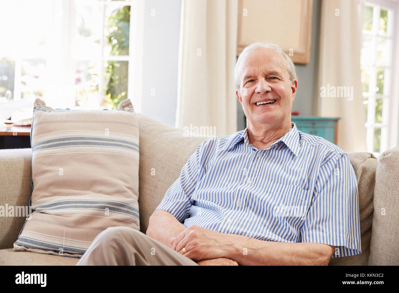 Portrait Of Smiling Senior Man Sitting on Sofa At Home Banque D'Images