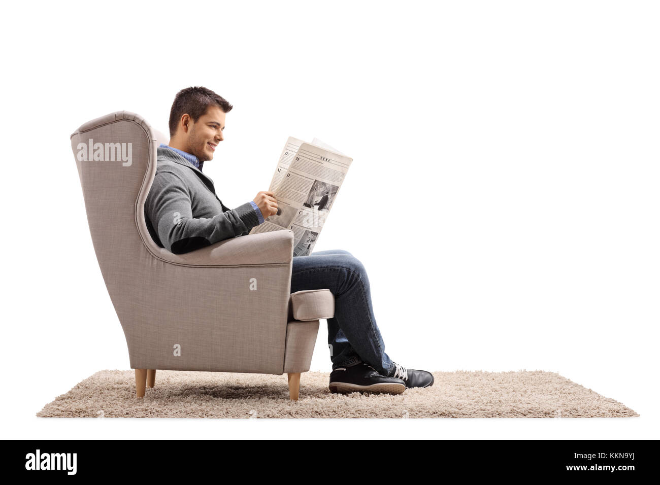 Jeune homme assis dans un fauteuil lisant un journal isolé sur fond blanc Banque D'Images