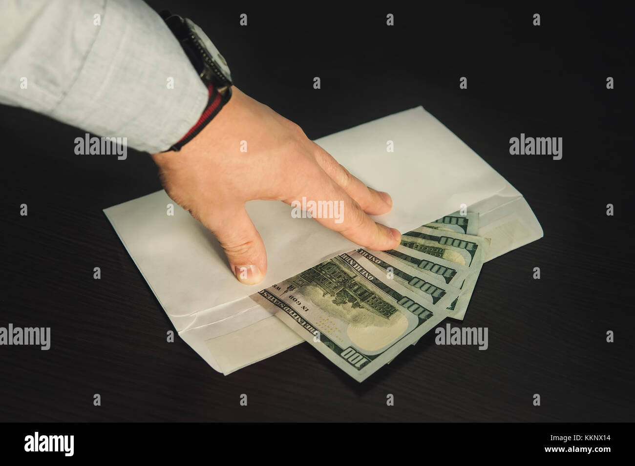Main tenant ses doigts masculins sur l'enveloppe blanche pleine de dollar américain, USD, euros, sur la table en bois en tant que symbole de transfert de l'argent illicite ou Banque D'Images