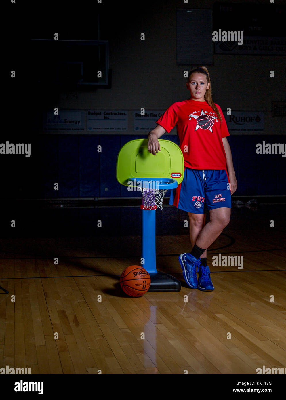 Un grand high school girl's basketball player pose à côté d'un bambin jouer hoop dans une salle de sport à souligner sa taille. Banque D'Images