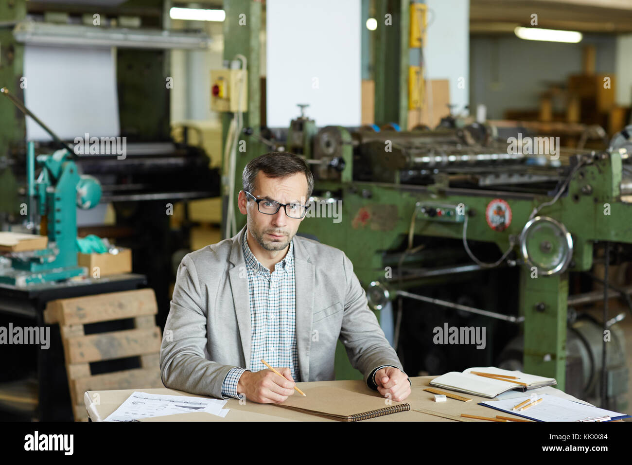 Ingénieur sérieux avec le bloc-notes et crayon à dessiner par son lieu de travail en usine Banque D'Images