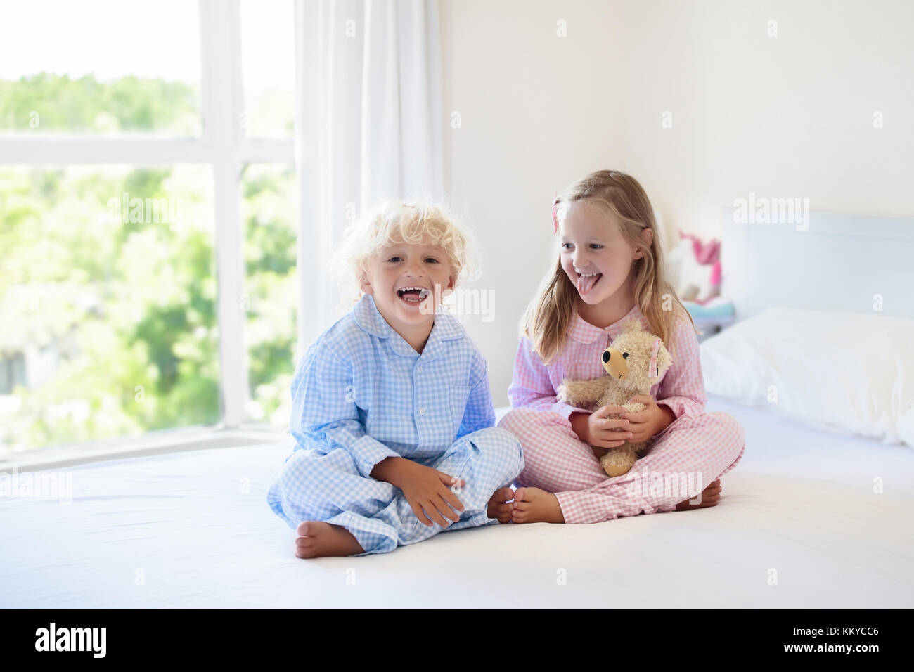 Les enfants jouaient dans la chambre des parents. Les enfants service en chambre blanche ensoleillée. Garçon et fille jouer en pyjama. vêtements ou de literie pour enfant et bébé. Banque D'Images