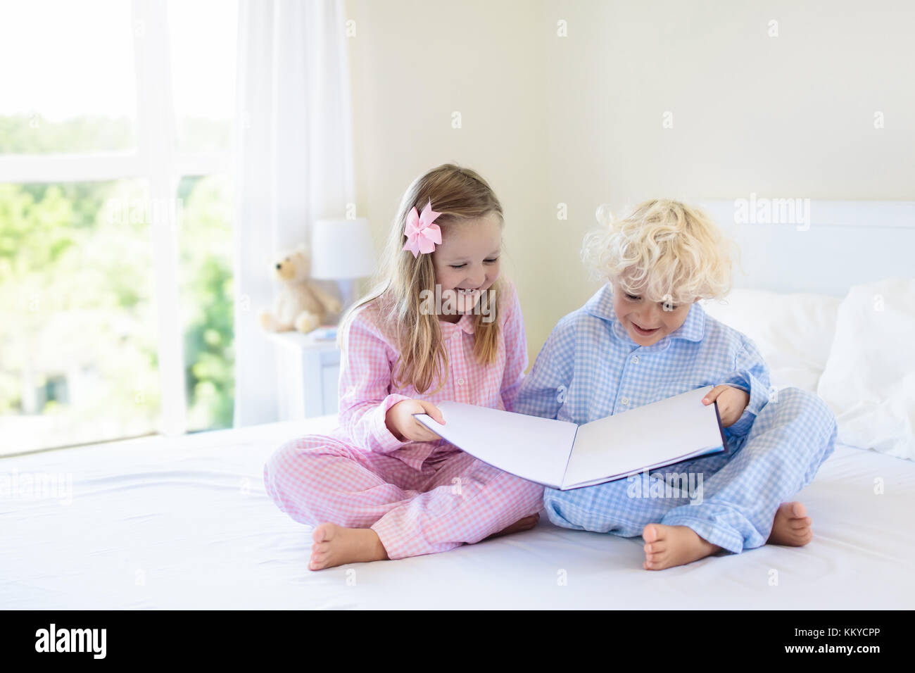 Les enfants jouaient dans la chambre des parents. Les enfants service en chambre blanche ensoleillée. Garçon et fille jouer en pyjama. vêtements ou de literie pour enfant et bébé. Banque D'Images