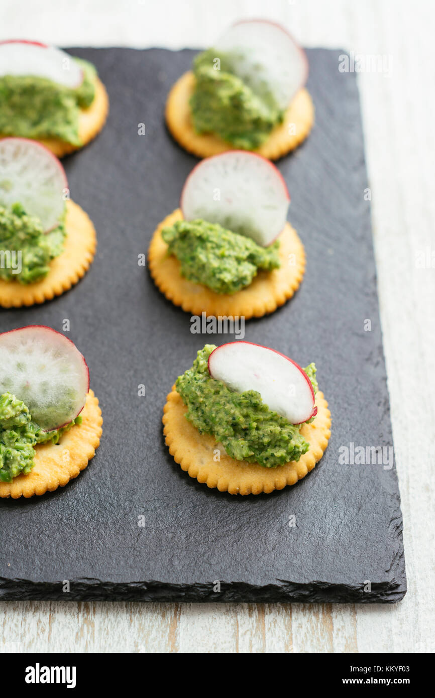 Radis et pois verts répartis sur des craquelins au pesto Banque D'Images