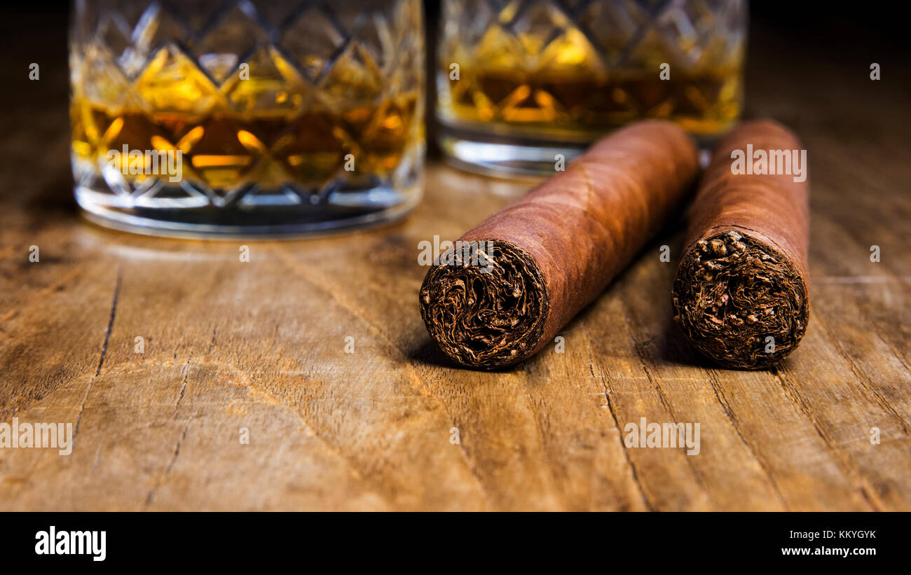 Deux cigares cubains avec deux verres de whisky sur une vieille table en bois avec un arrière-plan flou Banque D'Images