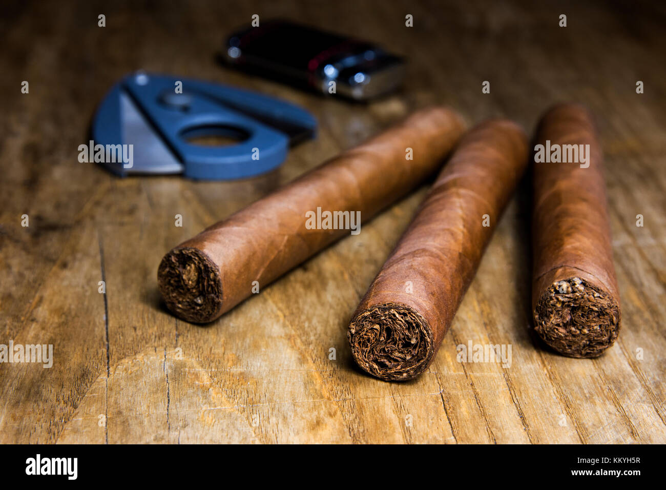 Trois cigares avec coupe-cigares et sur une vieille table en bois avec arrière-plan flou Banque D'Images