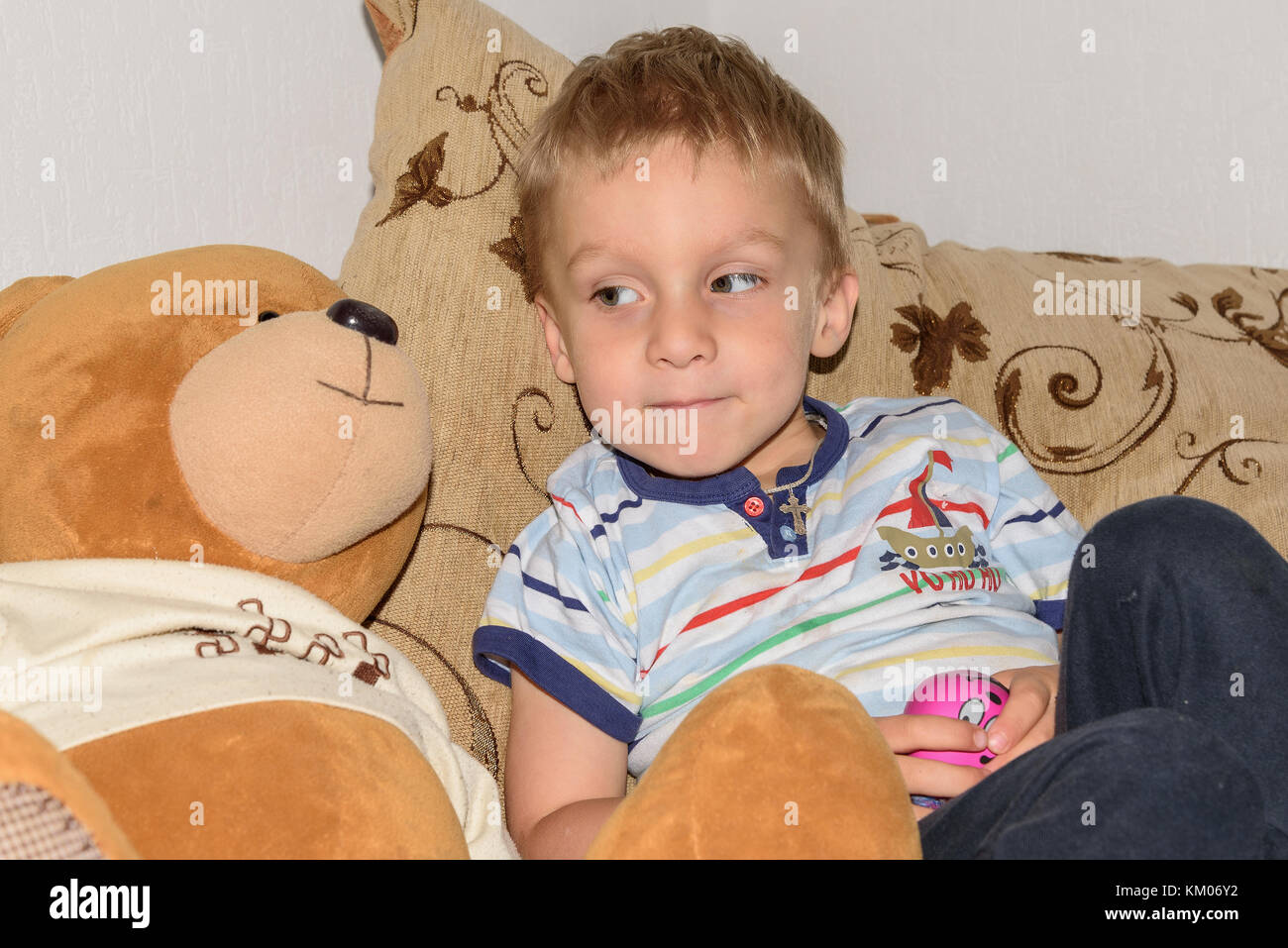 Portrait de petit garçon aux cheveux juste jouer avec la pâte à modeler et l'ours accueil sur le canapé Banque D'Images