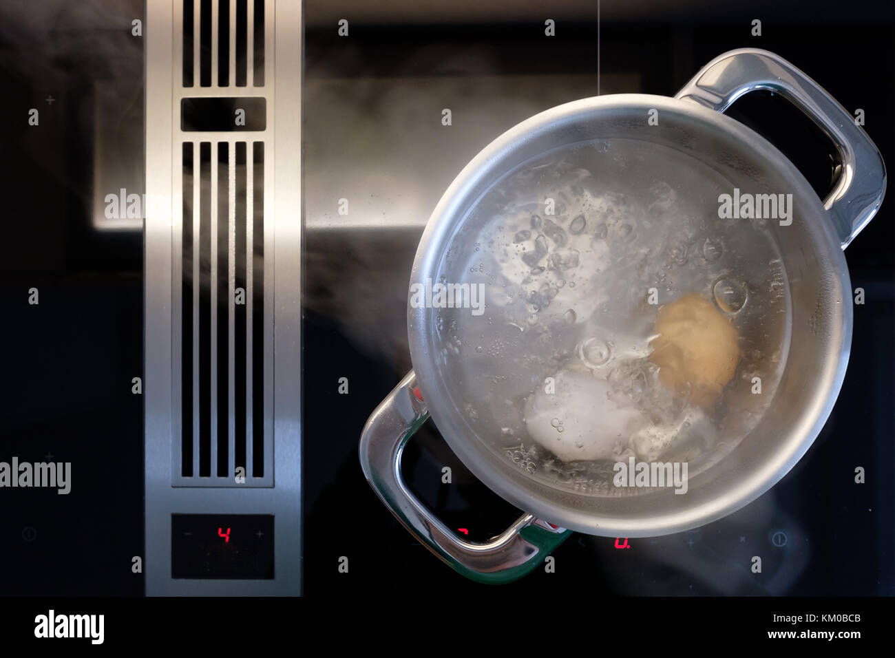 La cuisson des oeufs dans l'eau dans une casserole sur une cuisinière avec ventilateur d'extraction Banque D'Images
