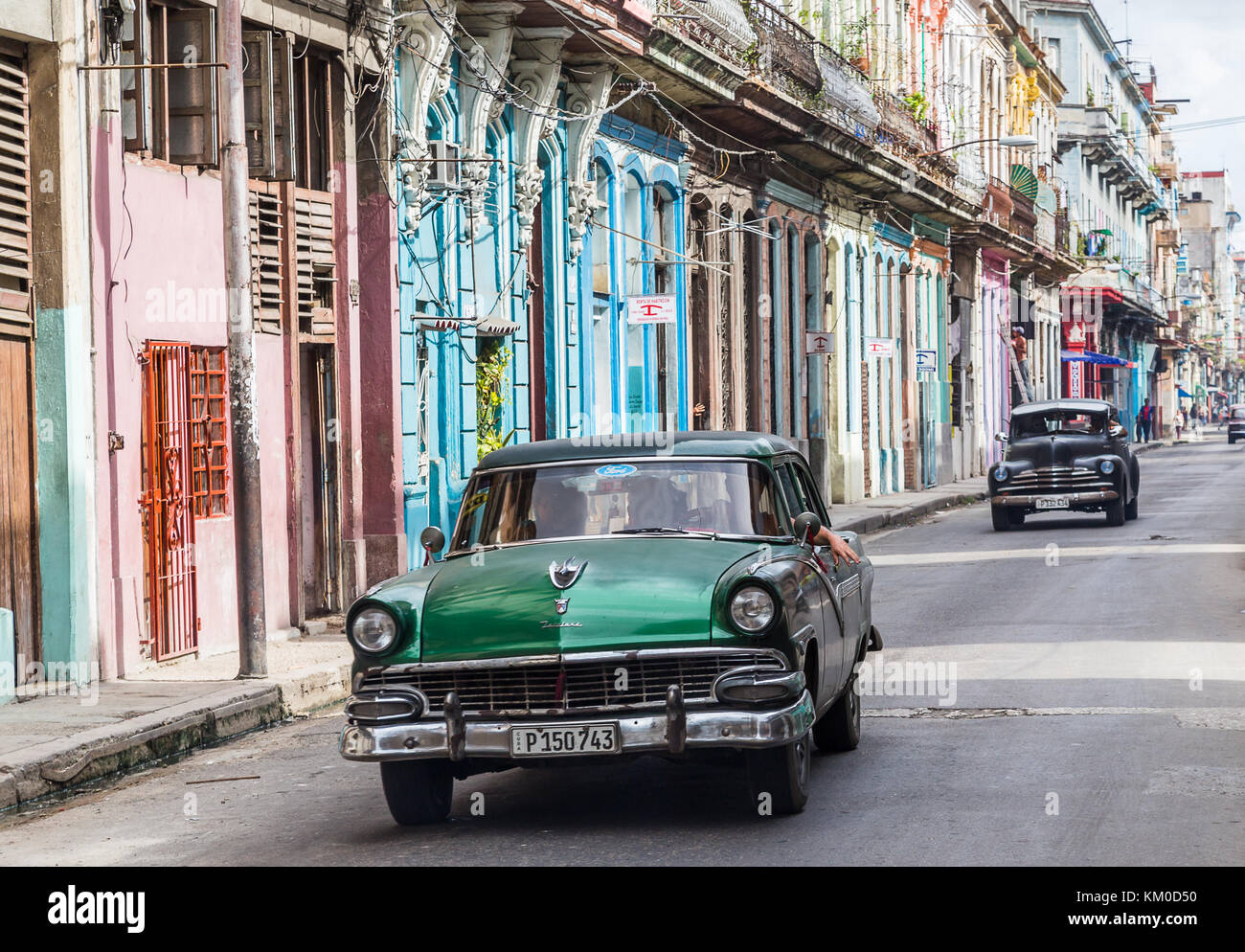 Une paire de vieilles voitures américaines des années 1950 voyage le long d'une rue colorée un matin de Centro Havana, le côté sauvage de la capitale cubaine, pendant Banque D'Images