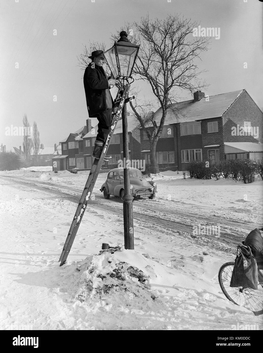 Image prise le 22 janvier 1963 dans le village de Staffordshire Pelsall, montrant un homme en haut d'une échelle, de l'éclairage l'éclairage des rues au gaz. Une scène d'hiver avec neige au sol et un Morris Monor voiture dans l'arrière-plan. Banque D'Images