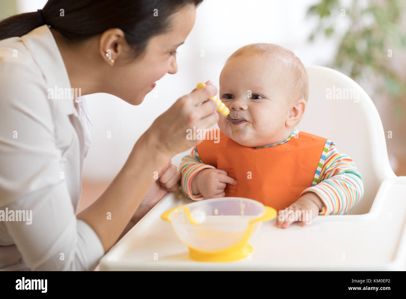 L'alimentation, de l'enfant et la parentalité concept - maman avec une cuillère de purée et nourrir bébé à la maison Banque D'Images