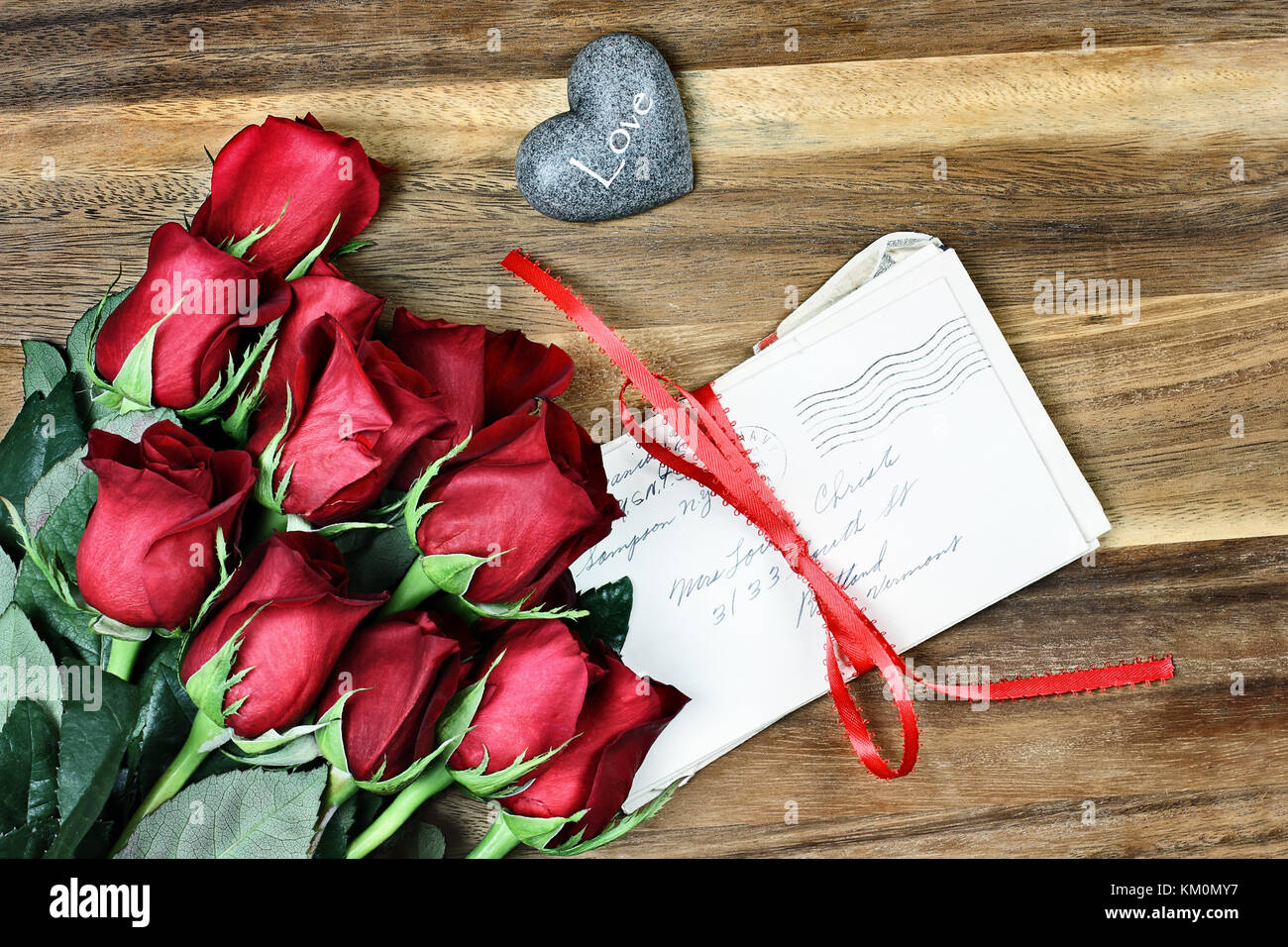 Longue tige roses rouges avec une pile de vieilles lettres attachées avec un ruban rouge et un peu de carte coeur de pierre avec le mot amour. Banque D'Images Longue tige roses rouges avec une pile de vieilles lettres attachées avec un ruban rouge et un peu de carte coeur de pierre avec le mot amour. Banque D'Images