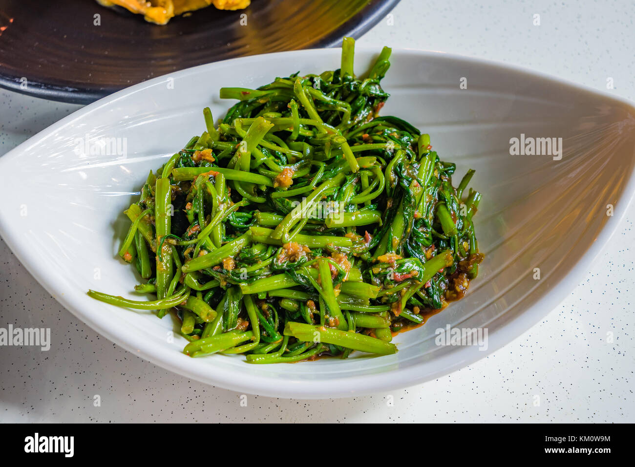 L'eau les épinards frits chinois avec l'ail et piment épicé de la sauce soja sur plaque blanche, à Singapour a appelé le sambal kangkong Banque D'Images