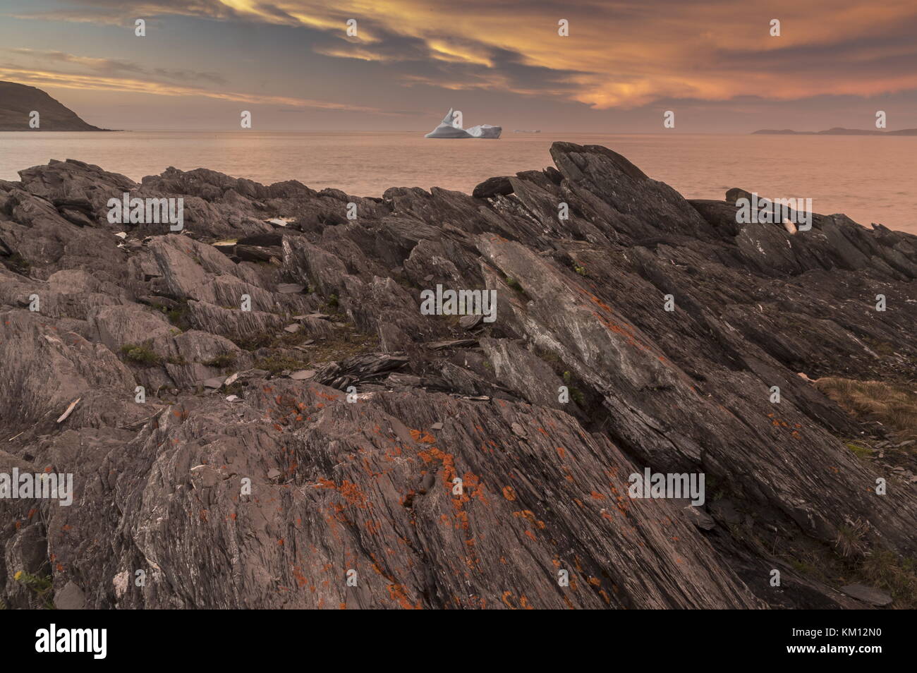 Iceberg au coucher du soleil, avec des roches couvertes de lichens, dans le détroit de belle Isle au large de la côte nord-ouest de Terre-Neuve. Banque D'Images