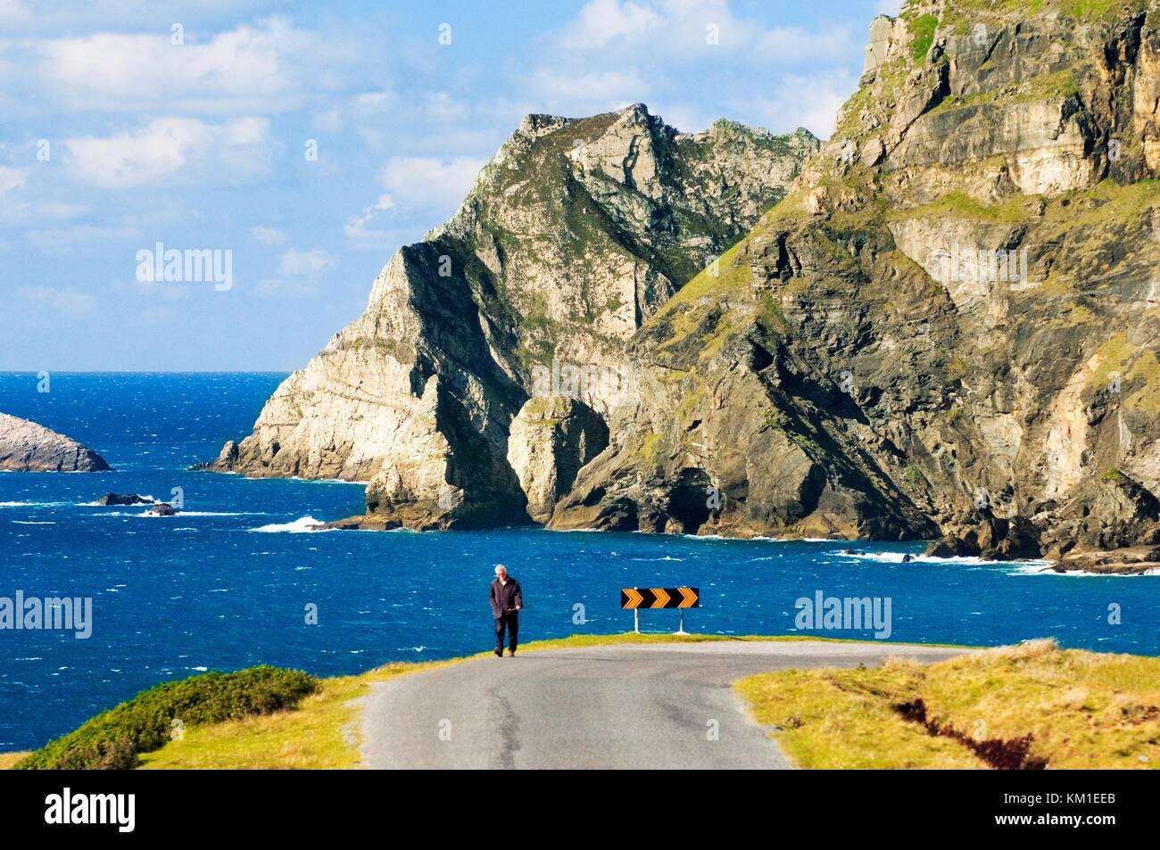 Homme marchant sur la route au sud de Greeneville à Malin Beg, le sud-ouest de comté de Donegal, Irlande. Falaises de Glen tête derrière. Banque D'Images